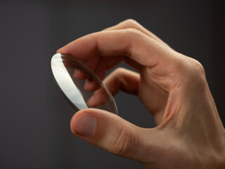 hand holding round glass lens for eyewear manufacturing quality control