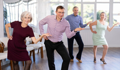 Happy senior woman and man enjoying active boogie-woogie dance in modern studio. Social dancing...