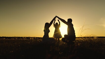 Figures of parents entwine hands above daughter amidst field. Silhouettes of parents holding hands...