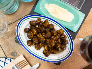 Cooked in shells land snails served on plate with spicy aioli sauce and glass of red wine. Popular...