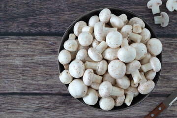 White button champignon mushrooms (agaricus bisporus) in a bowl with knife on wooden background. Top table view. Copy space.