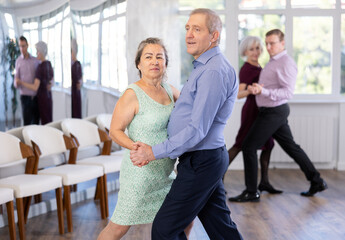 Senior man and elderly woman are dancing classic version of waltz in couple during lesson at...