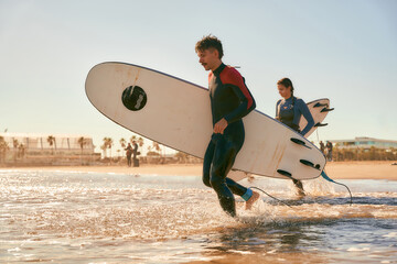 Side view of surfers in wetsuits running into the sea holding surfboards