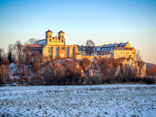 Tyniec near Krakow, Poland. Benedictine abbey and monastery on the rocky cliff at Vistula River in winter in sunset light - 715122854