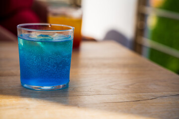 Standard Blue Lagoon cocktail on light grey table with ice cube and bubbles in a summer day