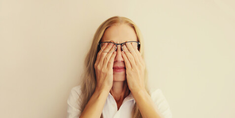 Tired overworked middle-aged woman employee rubbing her eyes suffering from eye strain, dry eye...