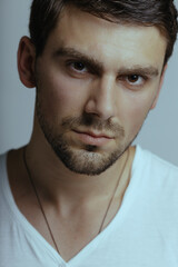 Fototapeta premium Fashion male studio portrait. Caucasian white guy with stubble. Large portrait of a guy in a white T-shirt.