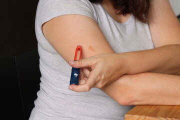 Woman applying insulin with insulin pen in her arm sitted in a chair. Woman applying insulin before...