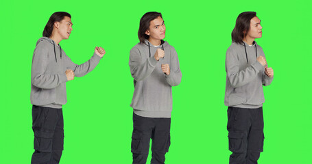 Young man throwing punches in the air, being violent and aggressive in studio. Asian person starting fight with fists, being furious and mad, dangerous behavior on greenscreen.