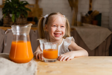Cute little blonde girl drinking fresh orange juice in the kitchen