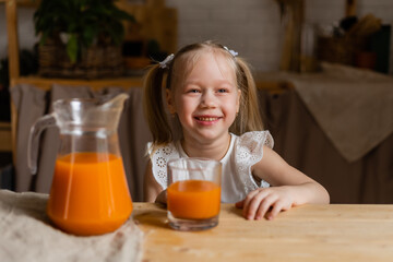 Cute little blonde girl drinking fresh orange juice in the kitchen