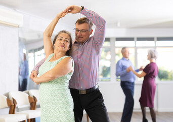 Middle-aged man and elderly woman are dancing classic version of waltz in couple. Leisure...