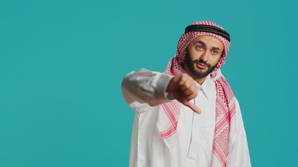 Muslim guy with ancient gown and kufiyah gives thumbs down and feels unsatisfied with stuff. Young...