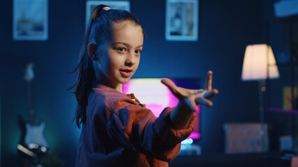 Close up shot of smiling kid dancing in dimly lit home studio interior, producing content for...