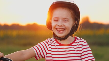 Girl with lost tooth stands with laughter in field. Girl wearing helmet stands laughing echoing...