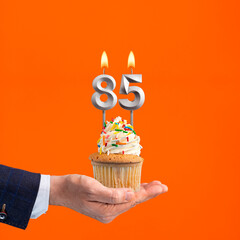 The hand that delivers cupcake with the number 85 candle - Birthday on orange background