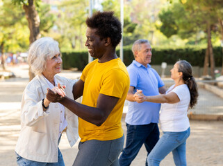 A troupe of cheerful multiracial amateur dancers of different age performing a partner dance outdoors in city park with one couple dancing in the foreground and the other behind