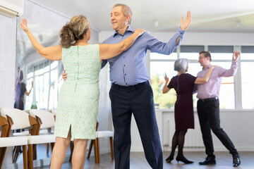 Senior man and elderly woman are dancing classic version of waltz in couple during lesson at studio. Leisure activities and physical activity for positive people.