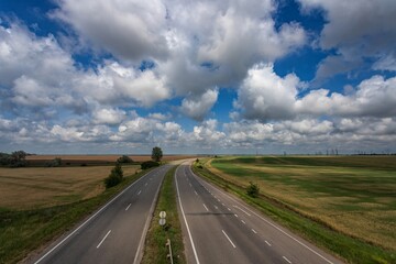 Fototapeta na wymiar Highway among fields under a beautiful sky with white clouds