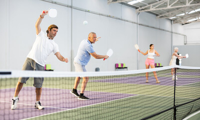 Athletic men playing pickleball tennis on the pickleball court indoors