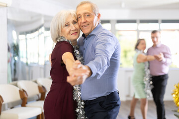 Against background of Christmas tree and decorations in studio, elderly couple enthusiastically dances rock and roll. Pleasant pastime and active hobby - obrazy, fototapety, plakaty
