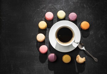 White cup of black coffee on a black background with colored macarons