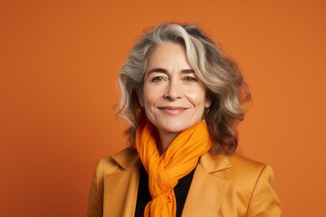 Portrait of smiling senior woman in orange scarf on orange background.