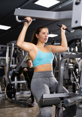 Fototapeta na wymiar Emotional athletic young girl working out on lat pulldown lever machine, performing back exercises. Fitness and weight training concept
