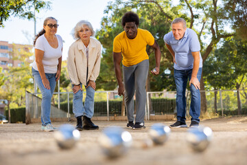 Company of friendly mature people playing petanque in park outdoor