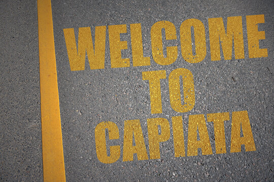 asphalt road with text welcome to Capiata near yellow line.