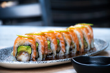 sushi maki roll of salmon avocado and sliced ​​shrimp and chopsticks in front close up with...