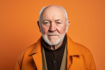 Portrait of an elderly man in a yellow coat on a orange background.