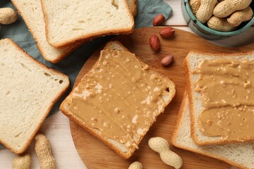 Delicious toasts with peanut butter and nuts on light wooden table, flat lay