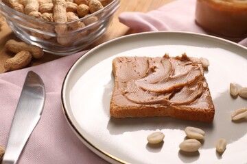 Toast with tasty nut butter, peanuts and knife on table, closeup
