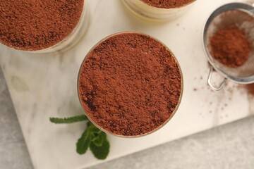 Delicious tiramisu in glasses and mint on grey textured table, top view