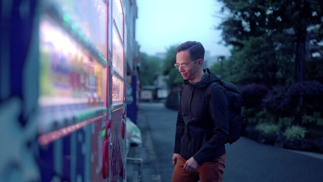 Side view of content Hispanic tourist male with backpack buying snack in vending machine on street in evening during vacation in Tokyo, Japan