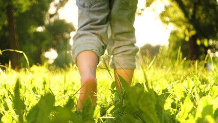 Small pleased child runs barefoot on grass in city park in warm weather. Boy sprints barefoot...