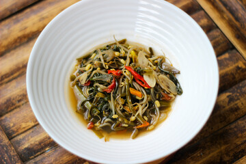 Stir fried kangkung or Indonesian food "tumis kangkung" served in a white bowl on a brown bamboo background