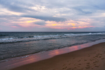 Pink sunset on the beach. Ocean, cloudy sky, and empty sandy beach at sunset