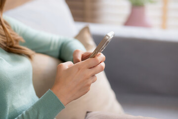 Closeup hand of happiness young asian woman sitting on sofa using smart phone with cozy in living room at home, happy woman on couch watching social media on smartphone with relax, lifestyles concept.