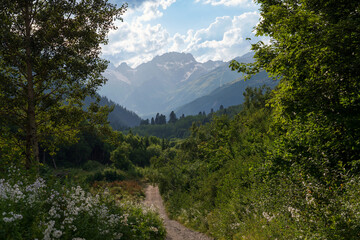 Obraz premium View of the Dombay-Ulgen gorge in the mountains of the North Caucasus and the trail to the Chuchkhur waterfall near the village of Dombay on a sunny summer day, Karachay-Cherkessia, Russia