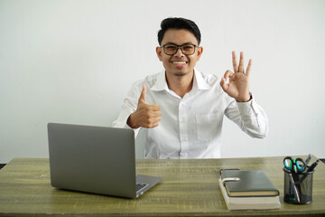 young asian businessman in a workplace showing ok sign and thumb up gesture, wear white shirt with glasses isolated