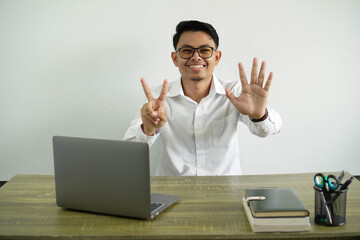 smiling young asian businessman in a workplace counting seven with fingers, wear white shirt with glasses isolated