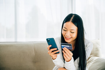 Fototapeta premium Woman on sofa uses smartphone and credit card for online shopping. Engaged in ordering banking and buying goods or services. Modern technology for convenient shopping at home.