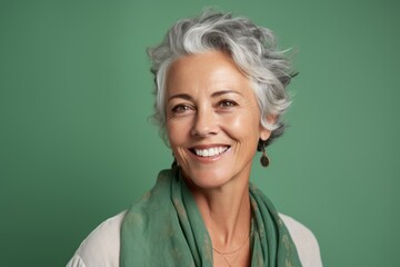 Portrait of smiling senior woman with grey hair against green background.