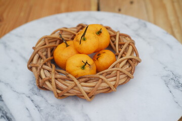 Yellow tangerines in a wicker basket on a marble table