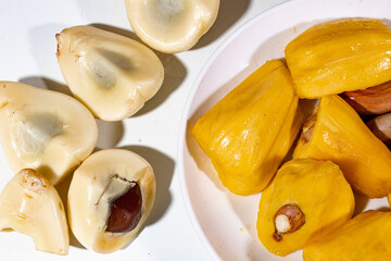 yellow jackfruit served on a plate, and peeled snake fruit, on a plain white background