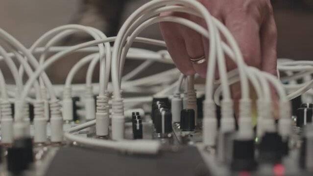 Closeup of unrecognizable hand of musician plugging multiple audio cables into professional modular synthesizer