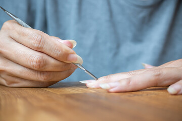 Woman using a cuticle pusher on her nails. Nail preparation process before applying polish. - obrazy, fototapety, plakaty