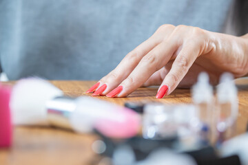 Close-up photo of a beautiful woman's hand with red painted nails on a table with nail accessories.